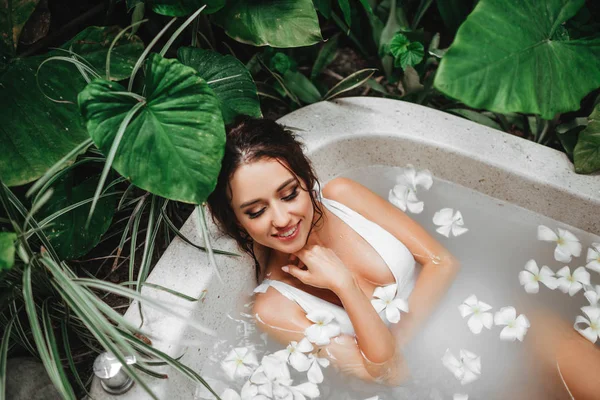 Femme relaxante dans un bain extérieur rond aux fleurs tropicales, soin de la peau bio — Photo