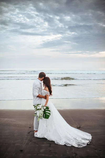 Elegante linda noiva e noivo andando na praia do oceano durante o pôr do sol . — Fotografia de Stock