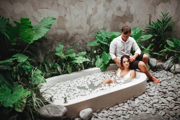 Žena a muž relaxují ve vaně s tropickými květy venku v luxusním hotelovém letovisku. — Stock fotografie