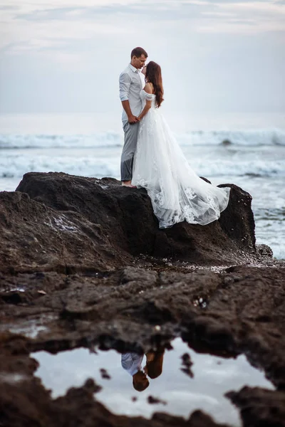 Elegante novia hermosa y novio caminando en la playa del océano durante la puesta del sol . —  Fotos de Stock