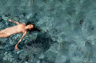 Yüzme havuzunda kolları açık yüzen çekici genç bir kadın.