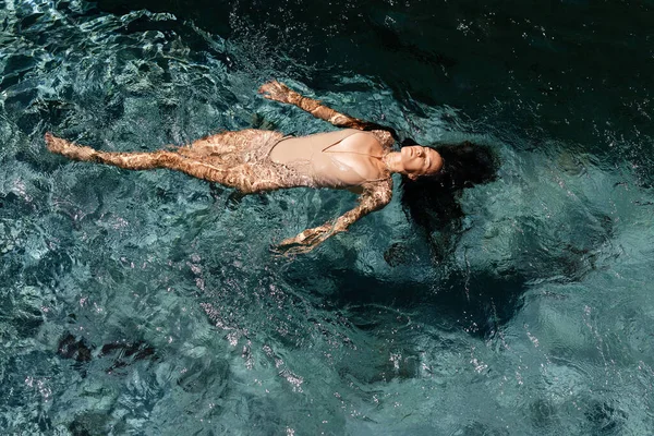 Atractiva joven flotando en una piscina con los brazos extendidos —  Fotos de Stock