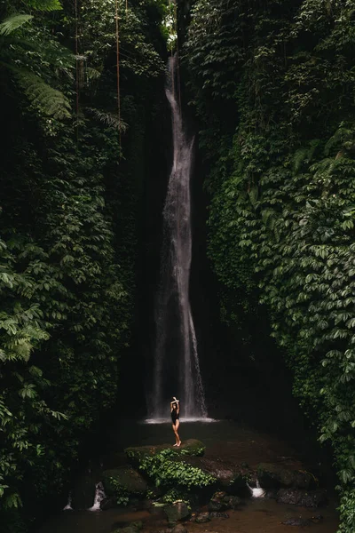 Jovem mulher mochileiro olhando para a cachoeira em selvas. — Fotografia de Stock