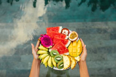 Otel havuzunun üzerinde servis edilen meyve tabağını tutan eller. Egzotik yaz diyeti.