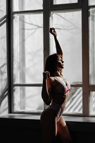 Mujer joven en ropa interior de encaje de pie junto a la ventana del dormitorio. — Foto de Stock