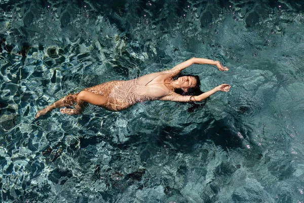 Attraktive junge Frau schwimmt mit ausgestreckten Armen im Swimmingpool — Stockfoto