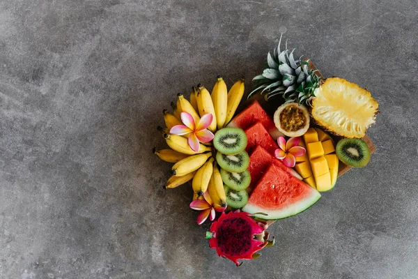 Surtido de frutas tropicales en un plato de madera. Fondo de piedra. — Foto de Stock