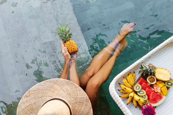 Mulher mão segurando abacaxi perto da bandeja com servido Café da manhã na piscina. — Fotografia de Stock