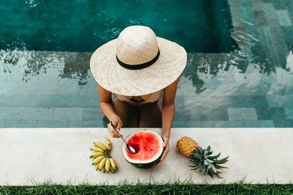 Chica relajante y comer frutas cerca de la piscina en villa de lujo en Bali. —  Fotos de Stock