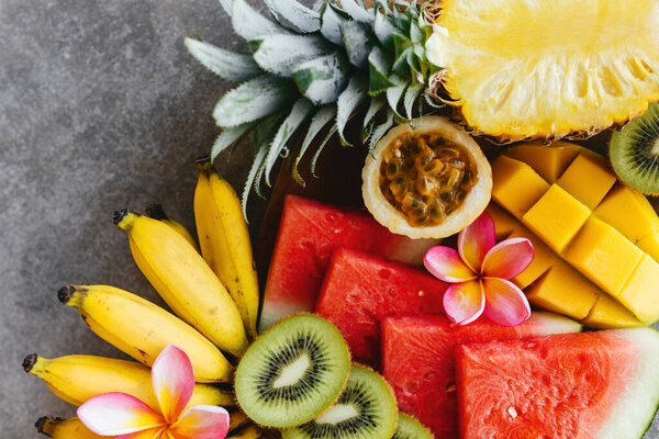 Tropical fruits assortment on a wooden plate. Stone background.