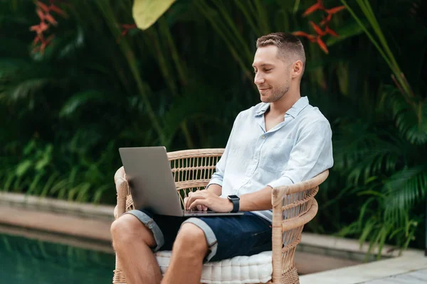 Mladý muž používající notebook v zahradě s bazénem. — Stock fotografie