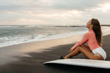 Okyanusta gün batımında beyaz sörf tahtası olan çekici genç bir sörfçü kadın. Bali Endonezya.