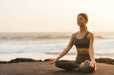 Sahilde gün batımında yoga. Kadın asanas gösterisi yapıyor ve okyanustaki hayatın tadını çıkarıyor.