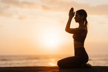 Sahilde gün batımında yoga. Kadın asanas gösterisi yapıyor ve okyanustaki hayatın tadını çıkarıyor.