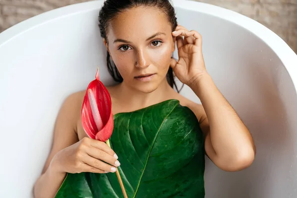 Portret van een jonge vrouw met anthurium bloem liggend in tropisch bad. — Stockfoto