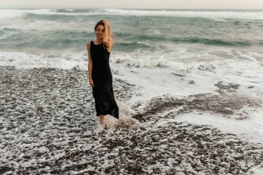 Kumsaldaki kadın, tatil boyunca sakin okyanus doğasının tadını çıkarıyor.