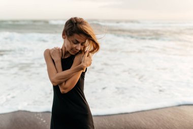 Kumsaldaki kadın, tatil boyunca sakin okyanus doğasının tadını çıkarıyor.