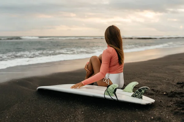 Mulher surfista atraente nova com placa branca no por do sol no oceano. Bali Indonésia. — Fotografia de Stock