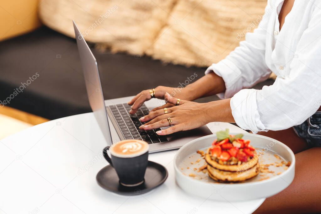 women hands at table with laptop near delicious pancakes with berries