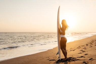 Gün batımında sahilde güzel bir sörfçü kadın