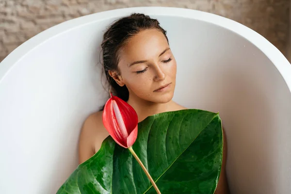 Retrato de uma jovem mulher com flor de antúrio deitada em banho trópico. — Fotografia de Stock