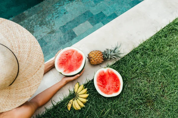 Joven mujer atractiva en la piscina disfrutando de deliciosas frutas tropicales maduras: sandía, plátanos y piña. —  Fotos de Stock