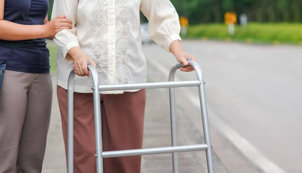 Senior vrouw met behulp van een walker cross street met verzorger — Stockfoto
