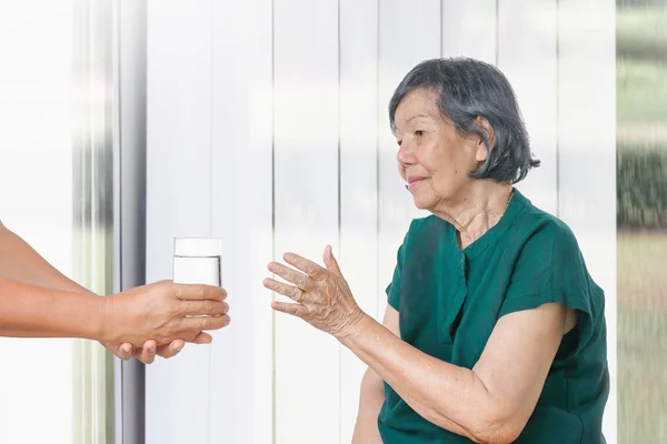 Elderly woman gets a glass of water from caregiver — Stock Photo, Image