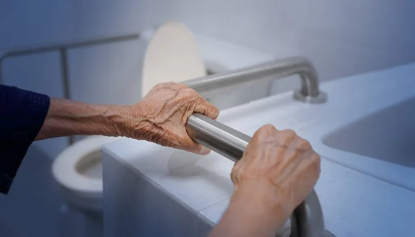 Elderly woman holding on handrail in bathroom — Stock Photo, Image