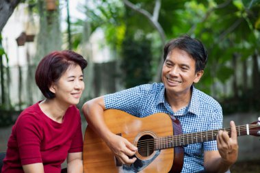 Orta yaşlı çift gitar çalarken rahatça arka bahçede bankta oturuyorlar..
