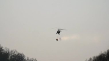 İtfaiyeci helikopter orman yangını için su kovası taşıyor.