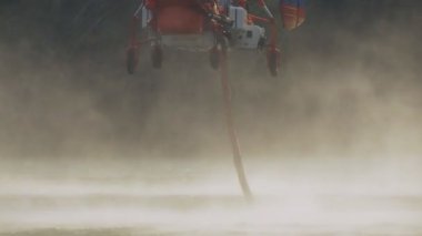 İtfaiye helikopteri su doldurmak için göletin üzerinde uçuyor.