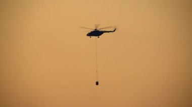 Siluet İtfaiye helikopteri orman yangını için su kovası taşıyor