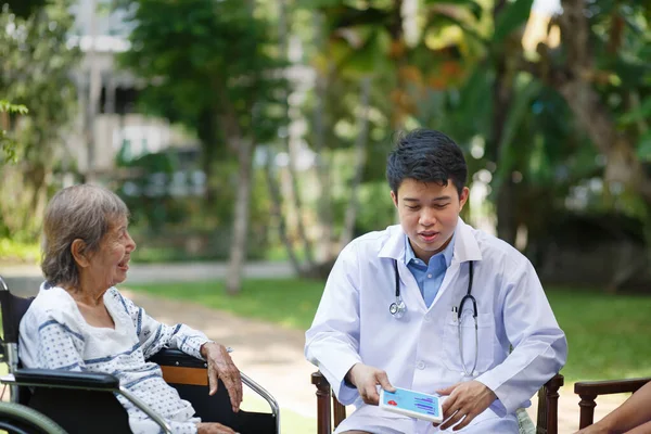 Asiatisk Læge Taler Med Ældre Kvindelig Patient Kørestol - Stock-foto