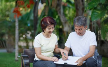 Asyalı orta yaşlı bir çift arka bahçede bahçe planlarını konuşuyor ve tasarlıyor..