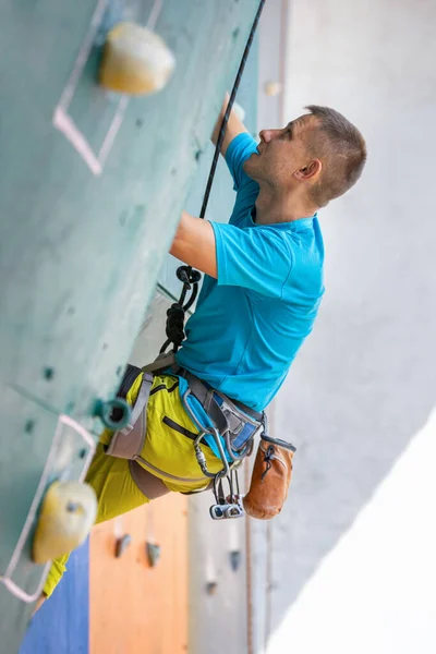 Młody człowiek wspina się na ścianę wspinaczkową — Zdjęcie stockowe