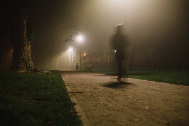 İnsanlar parkta, gece ve yoğun siste hareket bulanıklığı yaşıyor.