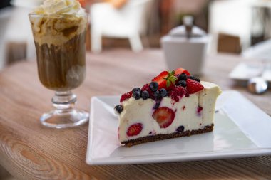 Cheesecake taze meyve ve arka planda buzlu kahve