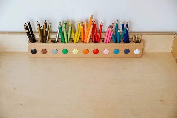 Farvede blyanter i en beholder på et træbord - Stock-foto
