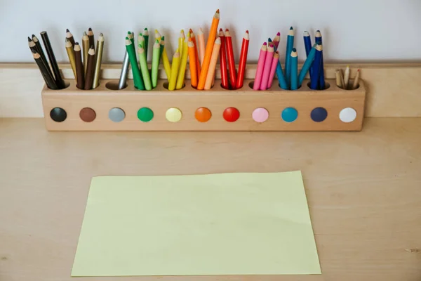 Lápis coloridos em um recipiente em uma mesa de madeira com papel — Fotografia de Stock