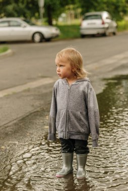 Kız lastik botlarla su birikintisinde oynuyor.