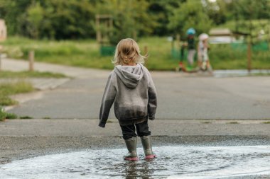 Kız lastik botlarla su birikintisinde oynuyor.