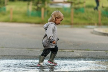 Kız lastik botlarla su birikintisinde oynuyor.