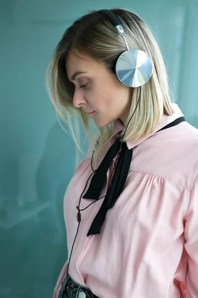 Linda loira em fones de ouvido de prata escuta música. Elegante — Fotografia de Stock