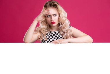 Sarışın kıvırcık saçlı ve parlak kırmızı dudakları ile şaşkın duygusal kız, boş bir beyaz arka plan yanında duruyor. Reklamınız, sunumunuz için yer.