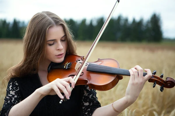 目を下にして小麦畑でバイオリンを弾く若い女性のクローズアップ肖像画 — ストック写真