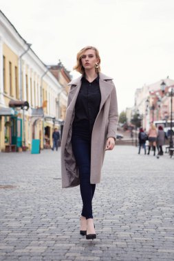 Sonbahar caddesinde yürüyen sonbahar montlu çekici sarışın kız.