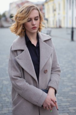 Portrait of a sad girl in a coat holding her handbag with both hands