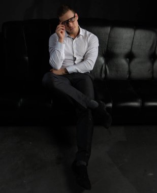 Beyaz gömlekli ve gözlüklü yakışıklı, kendine güvenen bir işadamı ofisteki koltukta oturuyor..