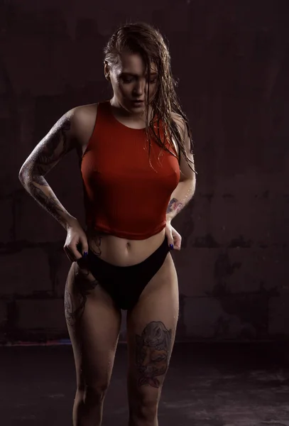 Μια πανέμορφη νεαρή γυναίκα σε ένα κόκκινο βρεγμένο μπλουζάκι ποζάρει σέξι σε ένα αμυδρά φωτισμένο στούντιο — Φωτογραφία Αρχείου